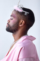 male princess in crown and cute pink outfit posing looking pretty, feminine transgender transvestite. attractive guy of black american ethnicity with make-up comsetics on face. side view, profile