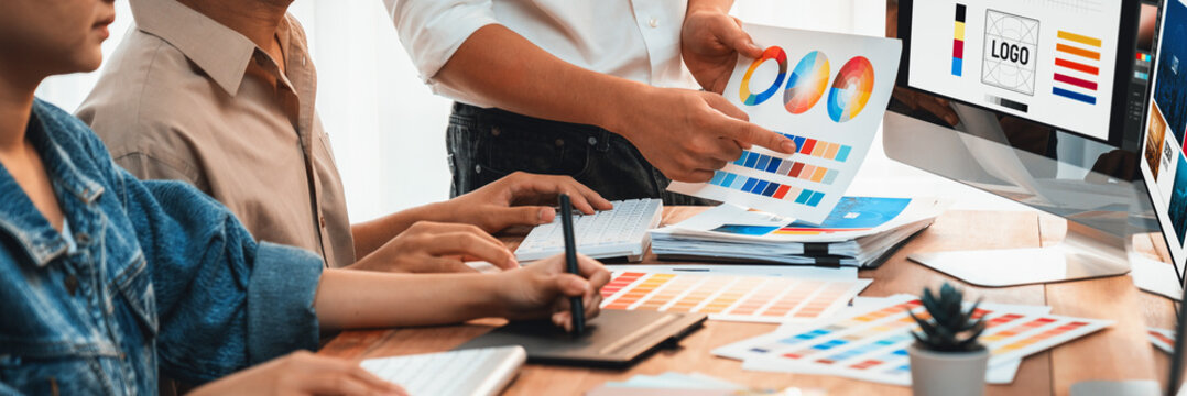 Graphic designer work on computer laptop and with graphic drawing pen while brainstorming unique design with professional graphic team in modern digital studio workplace. Panorama shot. Scrutinize