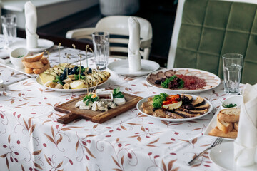 Served table food buffet in restaurant for wedding or birthday party dinner dishes. Assorted meats, chives, bacon, salami, hard cheese with mould, herbs, ananas, banana, grapes, fruits
