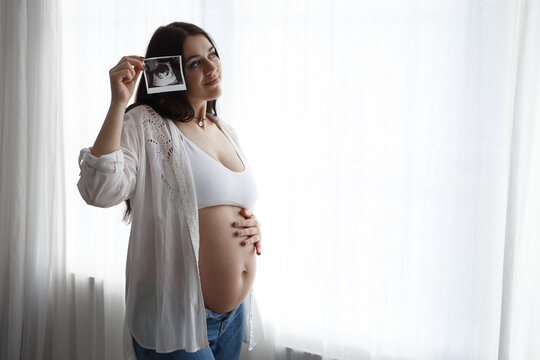 Pregnant woman standing hold strokes hold ultrasound photo of belly tummy fetus abdomen enjoying pregnancy. Future family, baby infant expecting child inside
