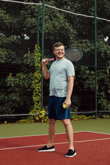 Cheerful young man in sportswear with a racquet standing on tennis court. Tennis player playing on a club hard court