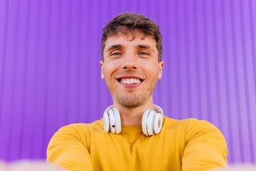 A young Hispanic student takes a selfie in yellow clothes on a purple background.