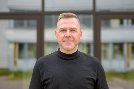 Man with gray hair in front of a glass office building