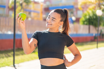 Young pretty brunette woman with an apple at outdoors with happy expression
