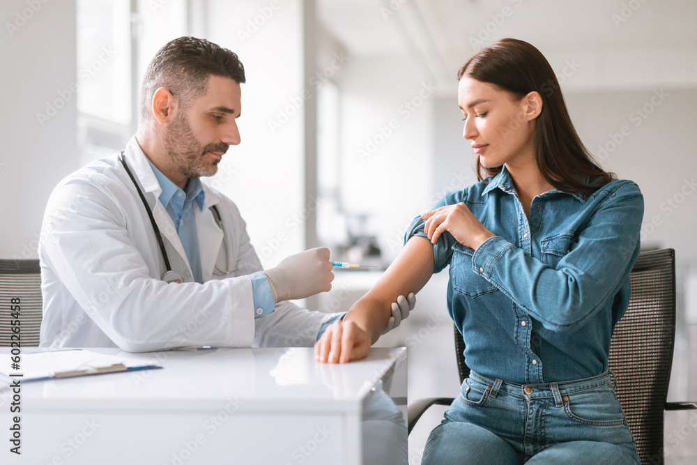 Wall mural Inoculation time. Doctor man wearing gloves and making vaccination shot to young female patient