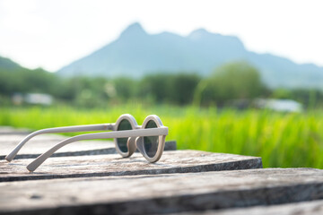 A sunglasses is placed on wooden floor with view of greenery rice field in the day time as...