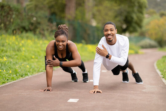 Happy young african american woman and guy doing push up exercise in park outdoor, free space