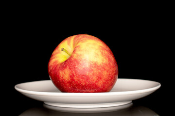 One ripe red apple on a white ceramic plate, macro, isolated on black background.