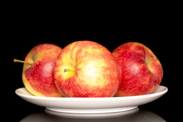 Three ripe red apples on a white ceramic plate, macro, isolated on black background.