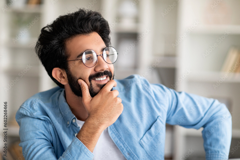 Wall mural Portrait Of Pensive Smiling Indian Man Wearing Eyeglasses Posing In Home Interior