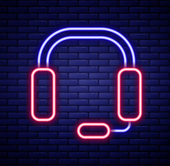 Glowing neon line Headphones icon isolated on brick wall background. Earphones. Concept for listening to music, service, communication and operator. Colorful outline concept. Vector