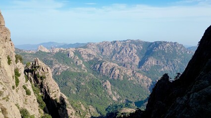 Naklejka premium Breathtaking Aerial Vista: A Journey Within the 'Trou de la Bombe', Aiguilles de Bavella, Corsica - Majestic Sunlit Peaks and Rugged Terrains Stretching into Infinity