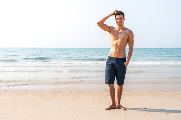 Portrait of smiling happy, relax handsome sexy man, male showing muscular fit body enjoying and relax standing on the tropical sea, beach.Summer vacations and travel