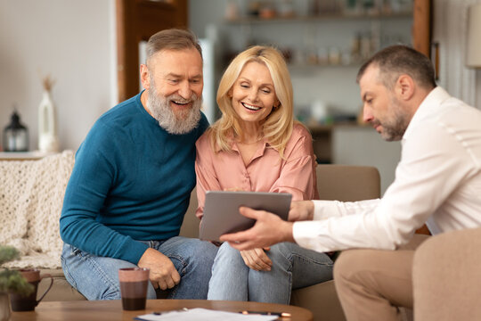 Professional Agent Showing Tablet To Excited Senior Couple At Home