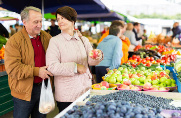 Aged man and woman customers buying apples in open-air market
