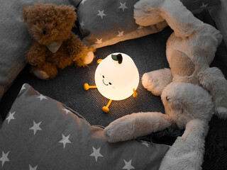 Kids' night light among pillows and toys. Turned on the night light. Cozy shelter for a little toddler. A cute flashlight that illuminates the nursery room.
