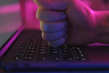 Human fist bump on the keyboard of laptop. Neon pink blue light. Failure concept. Playing video...