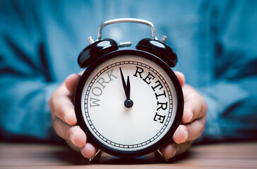 Businessman holding black alarm clock with clockwise countdown from work to retirement.