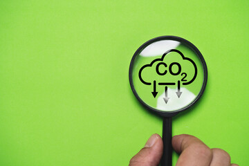 Hand holding CO2 reducing icon inside magnifier glass for focusing decrease CO2 or carbon dioxide emission ,carbon footprint and carbon credit to limit global warming from climate change concept. - obrazy, fototapety, plakaty