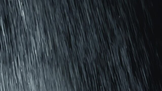 Heavy diagonal rain wall falling in front of the camera against the black screen— rain closeup vfx insert. Practical, seamlessly looped footage. Heavy rainstorm hitting black surface.	