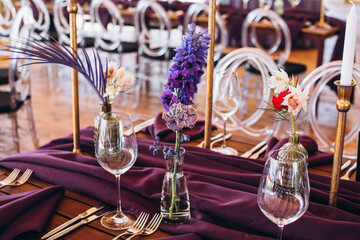 Wedding decor. Banquet. The tables are decorated with compositions of colorful flowers and greenery, violet tablecloths, candles, glasses, plates, and purple napkins.