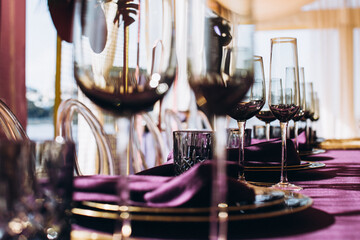 Wedding decor. Banquet. The tables are decorated with compositions of colorful flowers and greenery, violet tablecloths, candles, glasses, plates, and purple napkins.