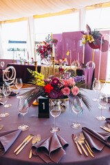 Wedding decor. Banquet. The tables are decorated with compositions of colorful flowers and greenery, violet tablecloths, candles, glasses, plates, and purple napkins.