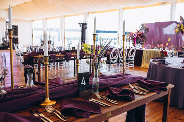 Wedding decor. Banquet. The tables are decorated with compositions of colorful flowers and greenery, violet tablecloths, candles, glasses, plates, and purple napkins.