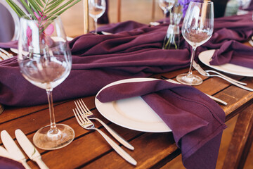 Wedding decor. Banquet. The tables are decorated with compositions of colorful flowers and greenery, violet tablecloths, candles, glasses, plates, and purple napkins.