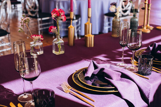 Wedding decor. Banquet. The tables are decorated with compositions of colorful flowers and greenery, violet tablecloths, candles, glasses, plates, and purple napkins.
