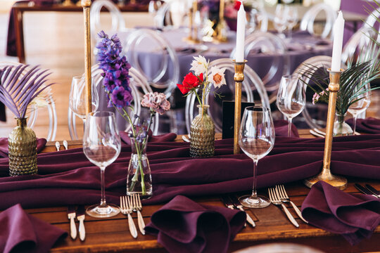 Wedding decor. Banquet. The tables are decorated with compositions of colorful flowers and greenery, violet tablecloths, candles, glasses, plates, and purple napkins.