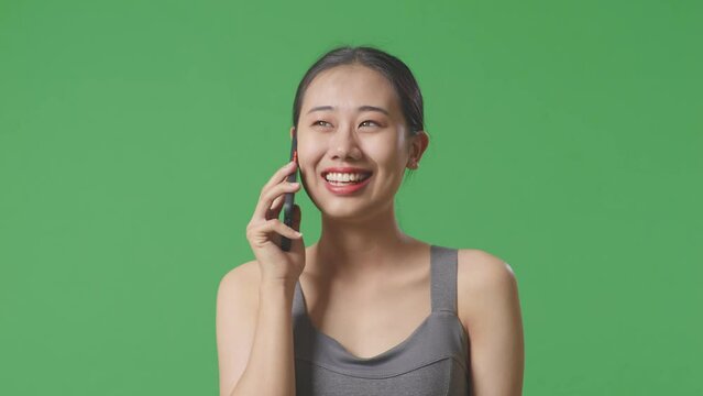 Close Up Of Asian Woman Wearing Sportswear And Taking Photo On Smartphone On Green Screen Background In The Studio
