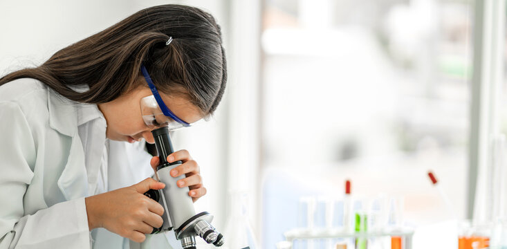 Cute little girl student child learning research and doing a chemical experiment while making analyzing and mixing liquid in glass at science class on the table.Education and science concept