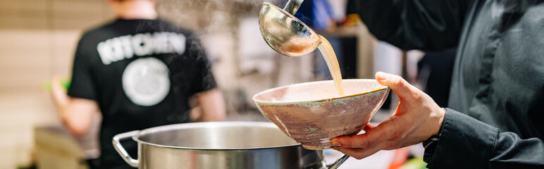 chef pouring tasty soup from big pot into bowl on restaurant kitchen
