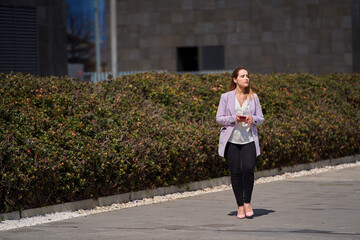 Businesswoman holding her mobile phone while walking outdoors. Business and technology concept.