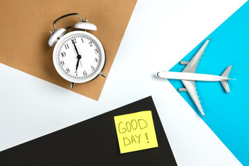 Alarm clock, paper reminder and airplane model on colored paper background.