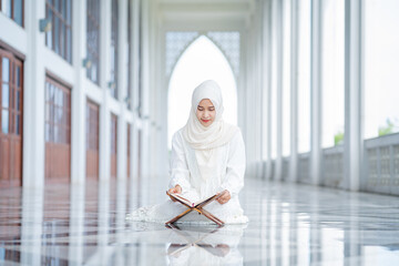 The image of an Asian Muslim woman in the Islamic religion in hijab in cream color. reading the...