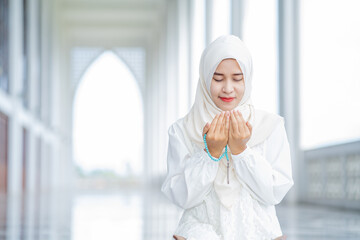 The image of an Asian Muslim woman in the Islamic religion in hijab in cream color. reading the...