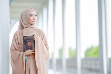 The image of an Asian Muslim woman in the Islamic religion in hijab in cream color. reading the...