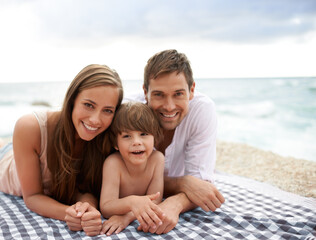 Beach, family and portrait outdoor in summer on a picnic blanket for travel vacation to relax. Smile of a man, woman and child or son happy together on holiday at sea with love, care and happiness