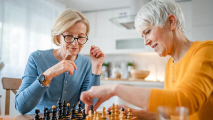 two women mature senior females sisters play chess board game at home