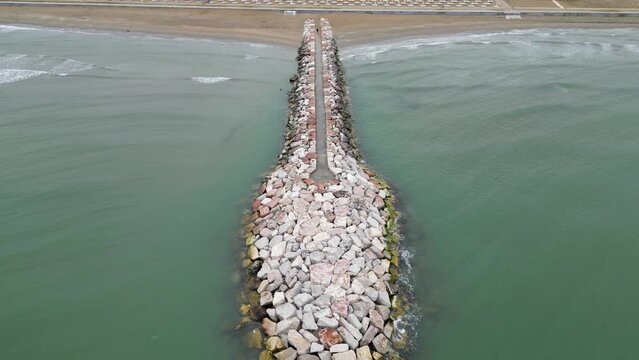 Smooth sea with beach and leaden rocks. Late spring, cloudy skies and rain to come. Italy, Veneto, shore of Eraclea