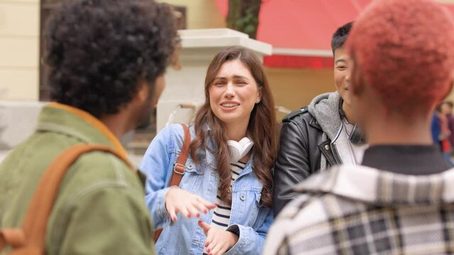 Close up of mixed-race people talking to happy beautiful Caucasian woman and Asian man outdoors. Cheerful young couple meet friends on street in city. Positive emotions, communication, fun concept