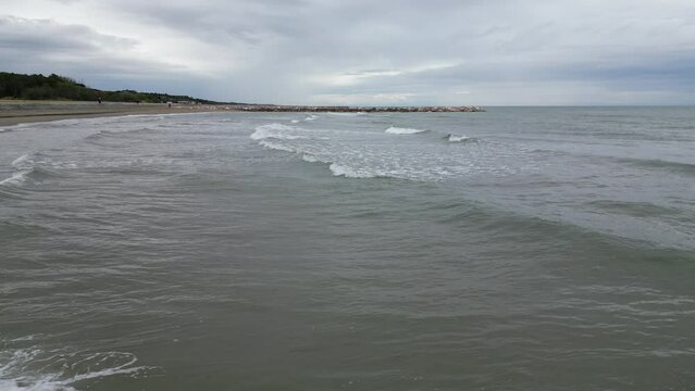 Smooth sea with beach and leaden rocks. Late spring, cloudy skies and rain to come. Italy, Veneto, shore of Eraclea