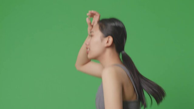 Side View Of Tired Asian Woman Wearing Sportswear And Running On Green Screen Background In The Studio
