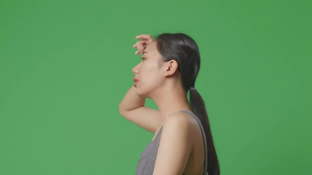 Side View Of Asian Woman Wearing Sportswear And Running On Green Screen Background In The Studio
