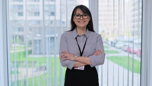 Middle aged woman with educational center badge with crossed arms, in office near window