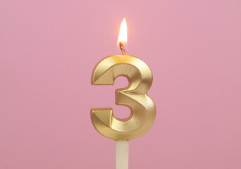 Golden birthday candle burning on pink background, number 3.