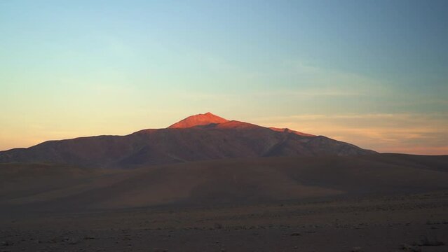 sunrise over the dry and arid Atacama desert in Chile, with golden and orange light falling onto a mountain.