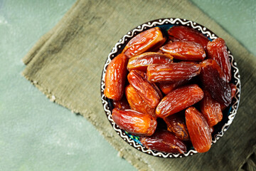 Bowl of pitted dates on a green linen napkin. Tasty sweet dried dates in bowl on a green background. Ramadan kareem